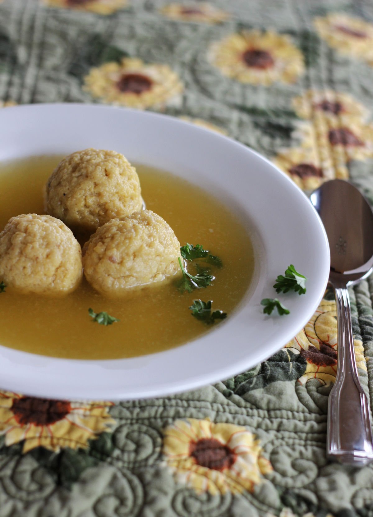 A bowl of matzo ball soup with three matzo balls in it.