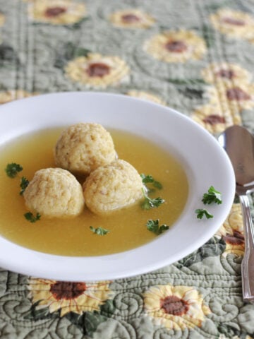 Three matzo balls in broth in a wide rimmed white soup bowl.