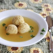 Three matzo balls in broth in a wide rimmed white soup bowl.