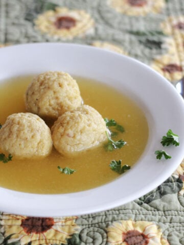 Three matzo balls in broth in a wide rimmed white soup bowl.