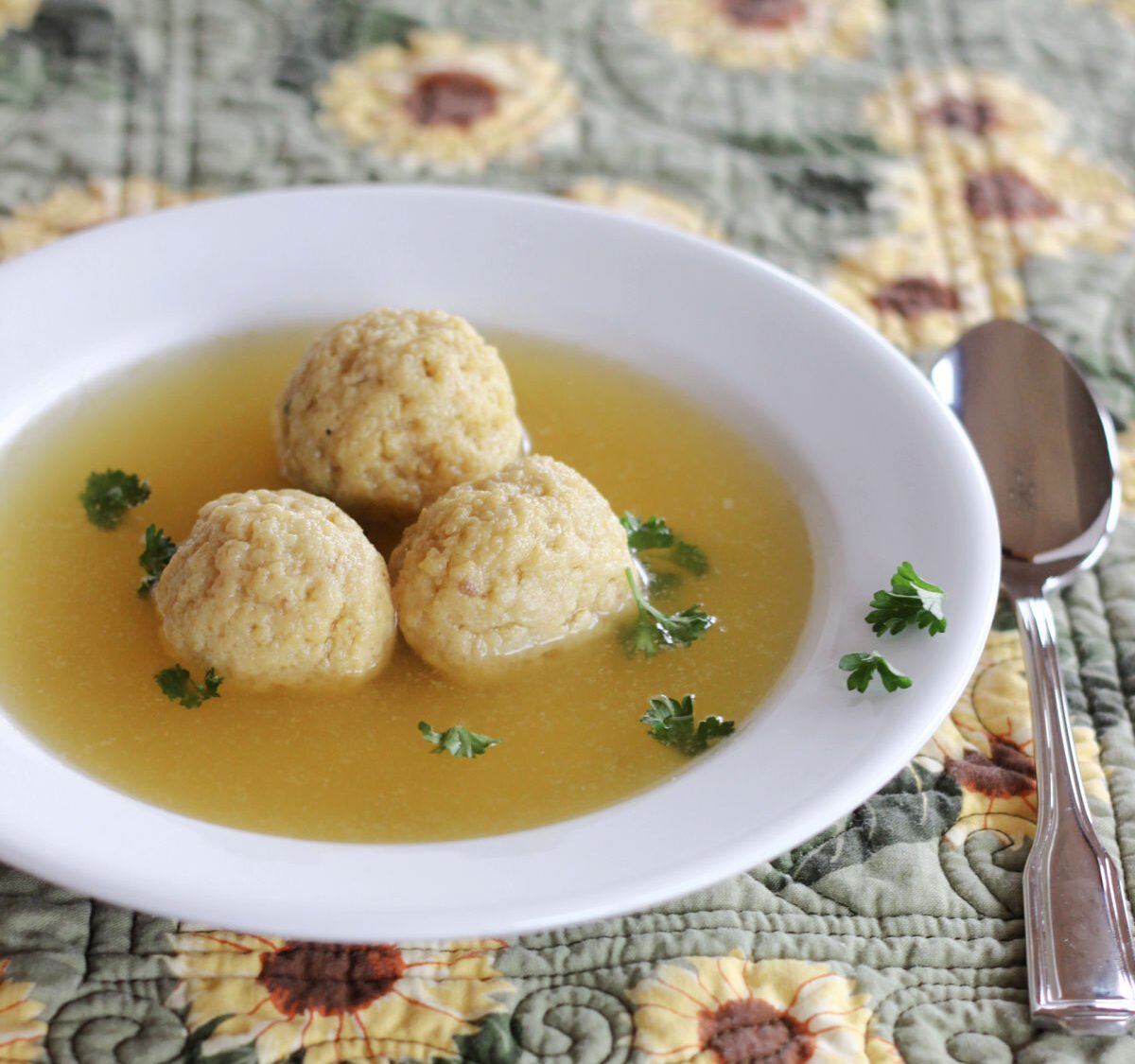 Three matzo balls in broth in a wide rimmed white soup bowl.