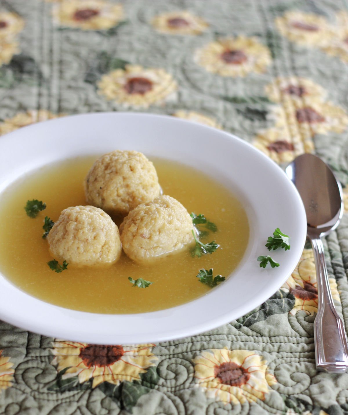 Three matzo balls in broth in a wide rimmed white soup bowl.
