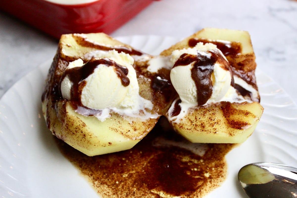 Two halves of apple with a cinnamony sauce with a scoop of ice cream on each apple half.
