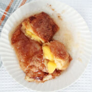 two peach dumplings on a white plate. One has been cut in half so the peach filling can be seen.