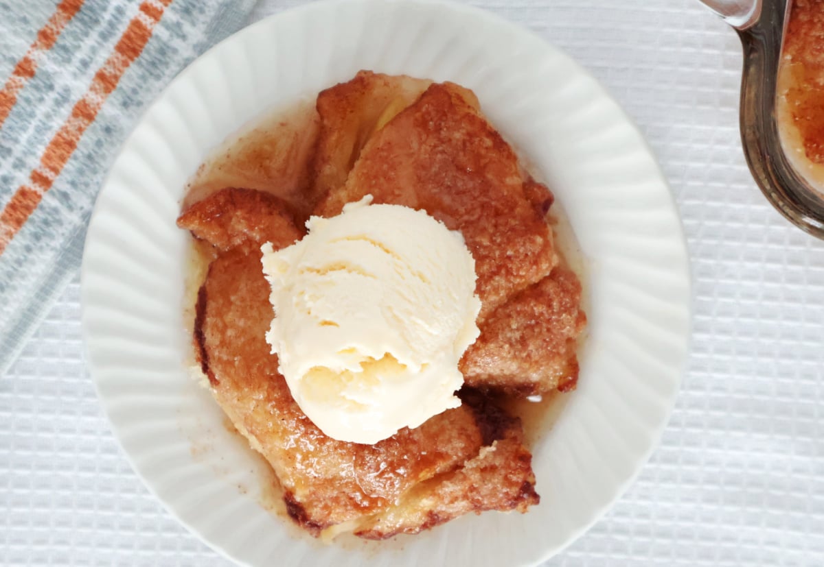 Two baked peach dumplings on a white plate. A scoop of vanilla ice cream is on top of the dumplings.