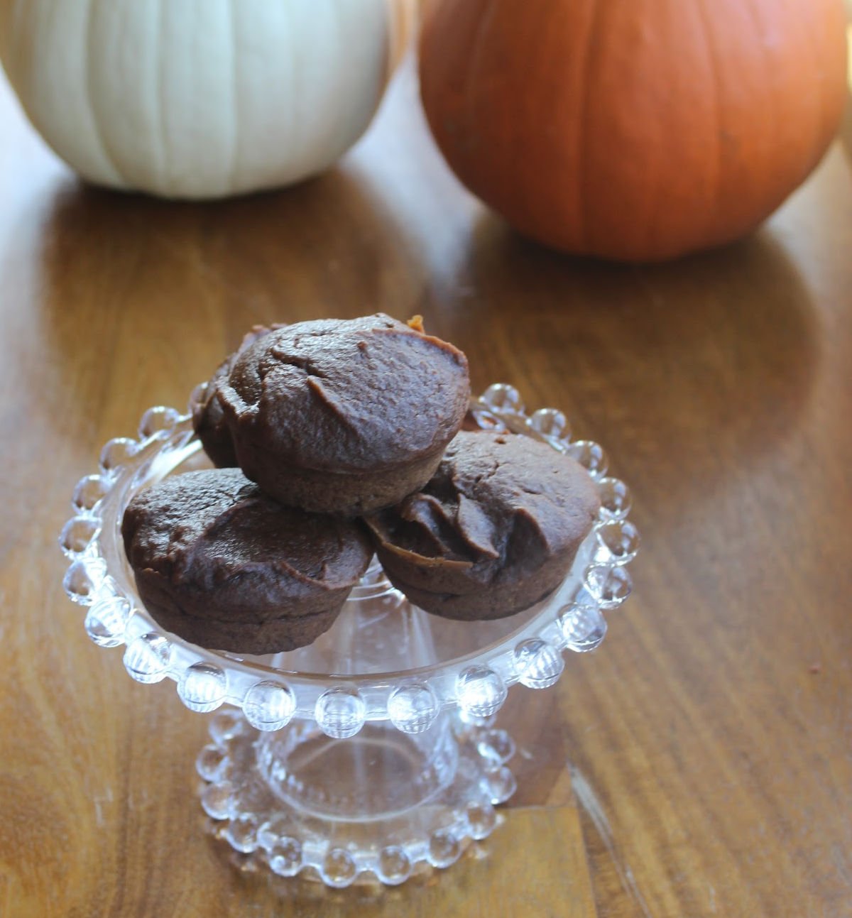 three pumpkin brownies on a clear glass tray with pumpkins in the background.