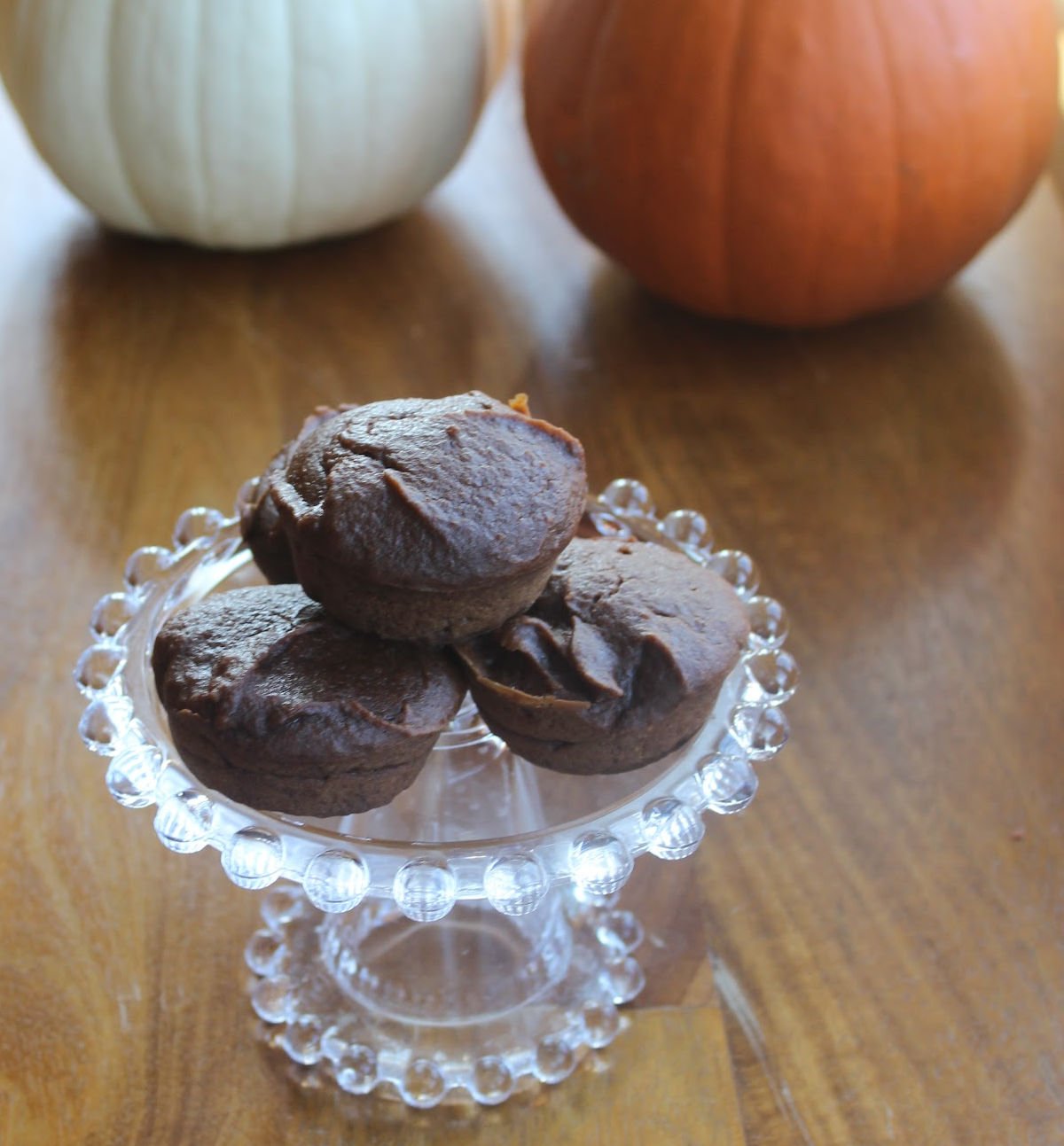 Three pumpkin chocolate brownies on a clear dish with a white and an orange pumpkin standing behind the dish.