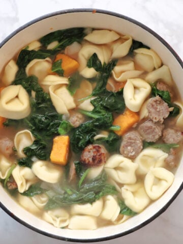 Sausage spinach tortellini soup with sweet potatos in a red dutch oven.