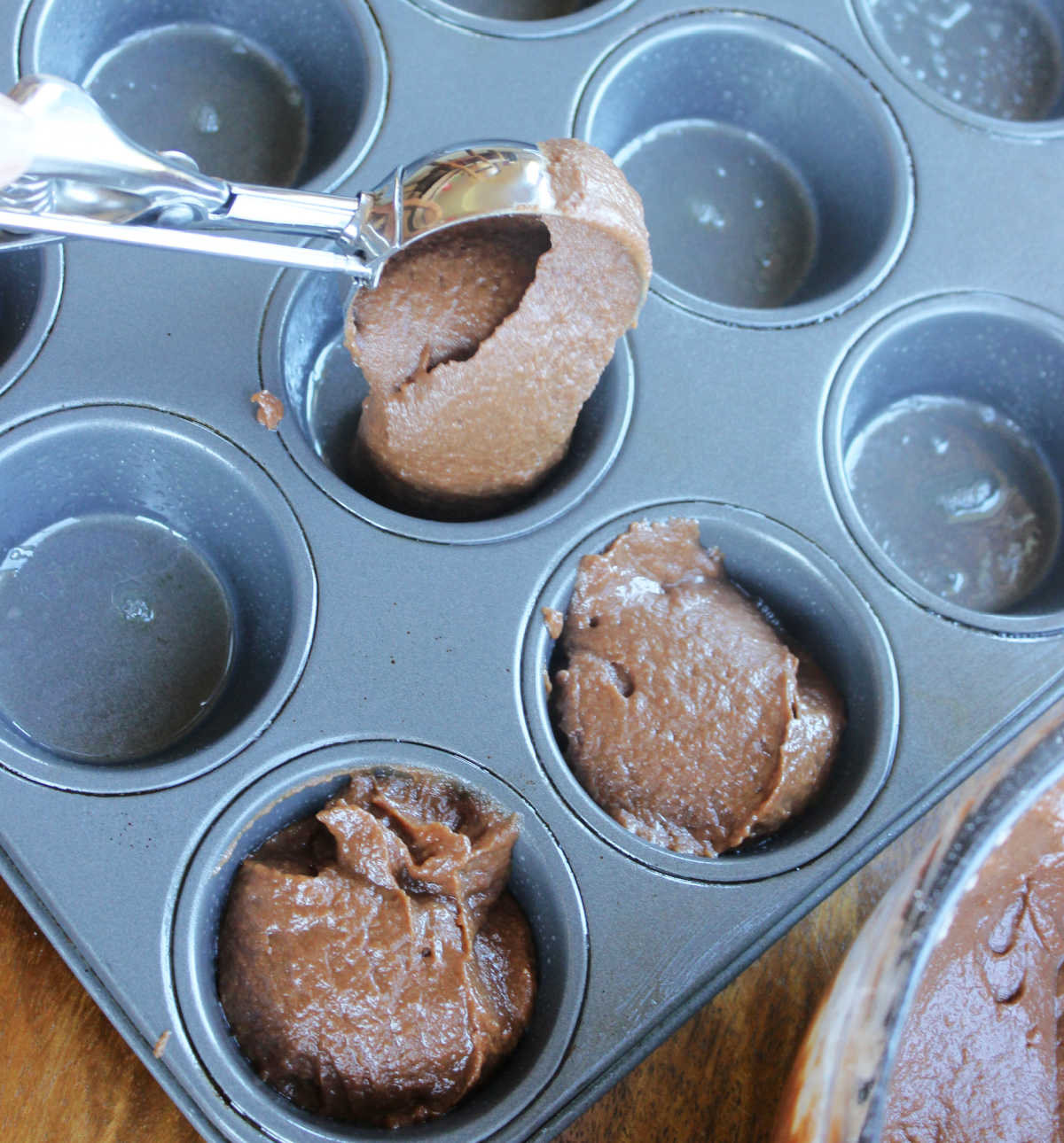 muffin batter is placed into muffin tin with scoop.