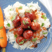 meatballs on top of a bed of rice with a sauce on the meatballs and some chopped parsley as the garnish. Roasted carrots are also on the plate