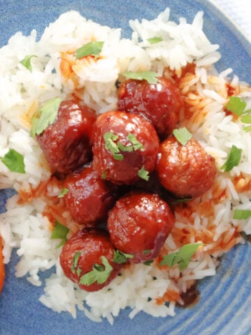 meatballs on top of a bed of rice with a sauce on the meatballs and some chopped parsley as the garnish. Roasted carrots are also on the plate