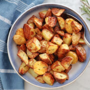 Air Fryer Rosemary Potatoes in a blue bowl with a sprig of rosemary beside the bowl.