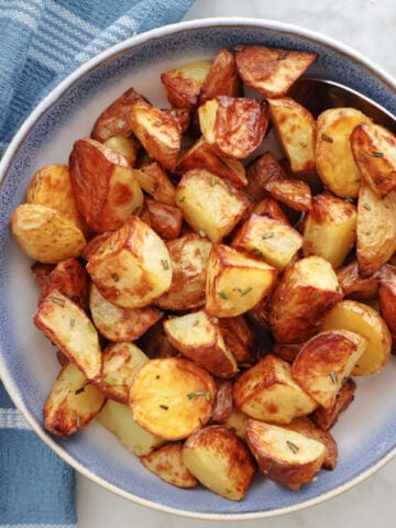 Air Fryer Rosemary Potatoes in a blue bowl with a sprig of rosemary beside the bowl.