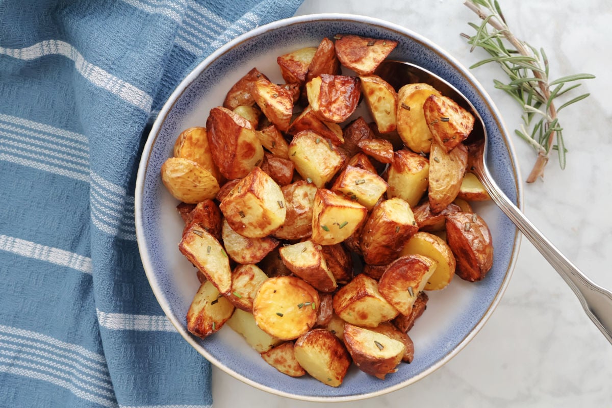 Air Fryer Rosemary Potatoes in a blue bowl with a sprig of rosemary beside the bowl.