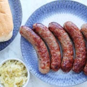 Air Fried brats on a plate with brat buns and sauerkraut to the side of the image.