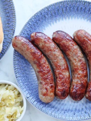 Air Fried brats on a plate with brat buns and sauerkraut to the side of the image.