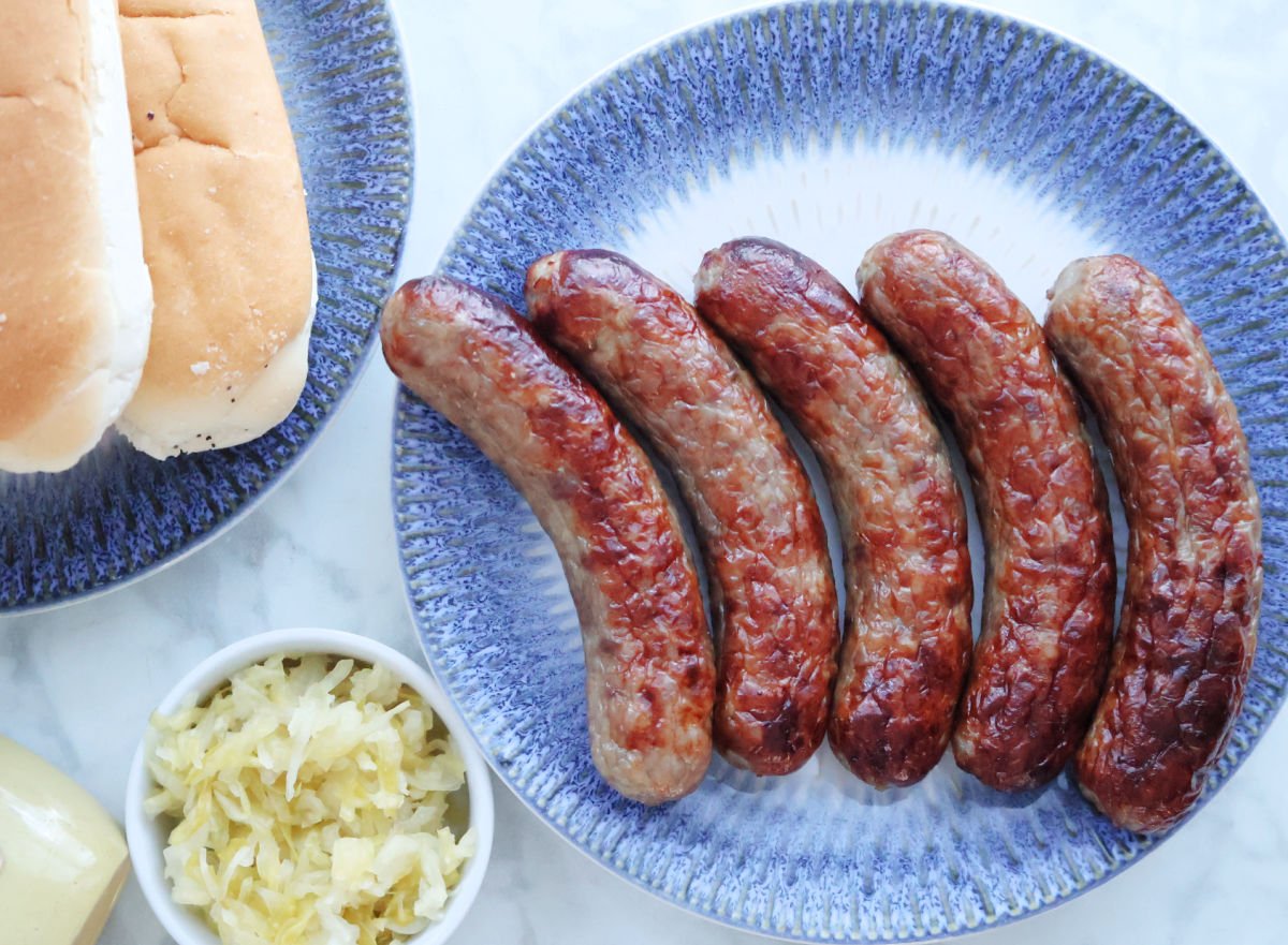 Air Fried brats on a plate with brat buns and sauerkraut to the side of the image.