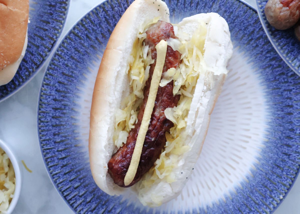 A brat in a brat roll garnished with sauerkraut and dijon mustard.