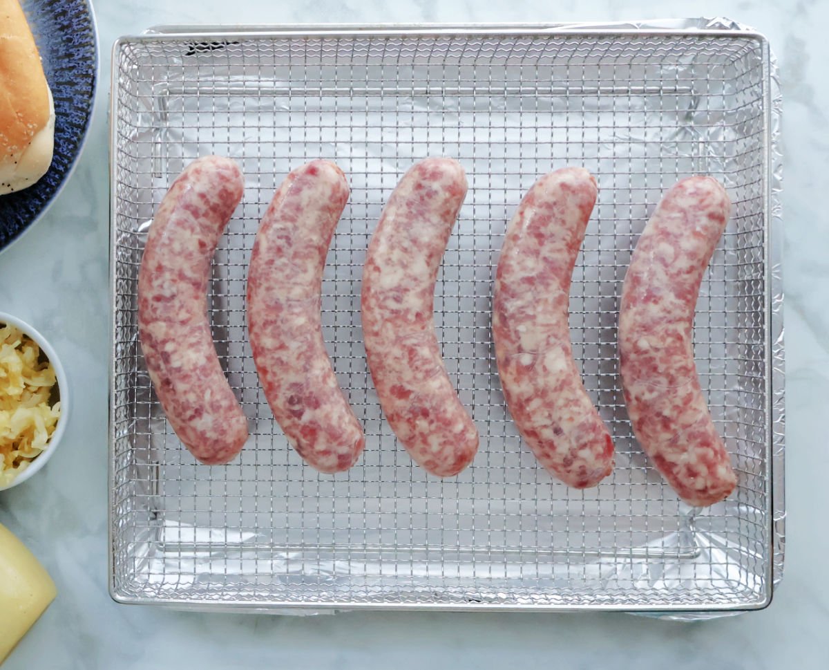 5 uncooked brats on an air fryer tray ready to be air fried.