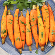 regluar sized roasted carrots on a blue plate. Carrots are roasted and has some parsley on them as garnish.