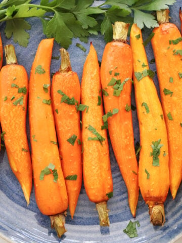 regluar sized roasted carrots on a blue plate. Carrots are roasted and has some parsley on them as garnish.