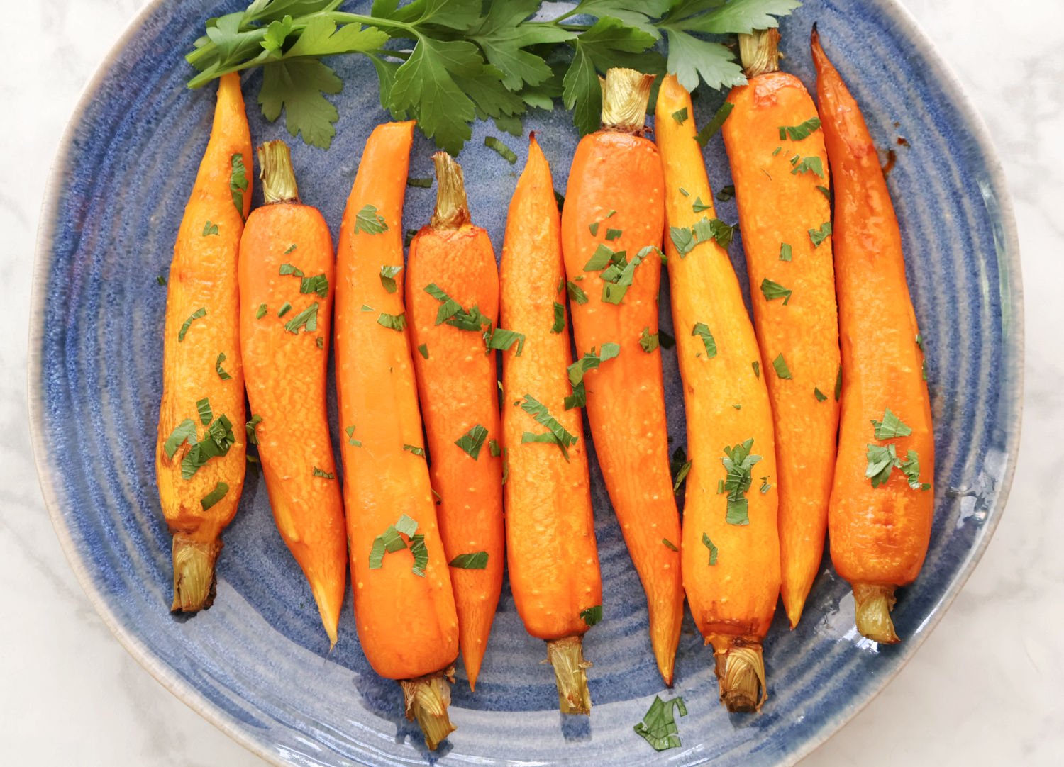 regluar sized roasted carrots on a blue plate. Carrots are roasted and has some parsley on them as garnish.