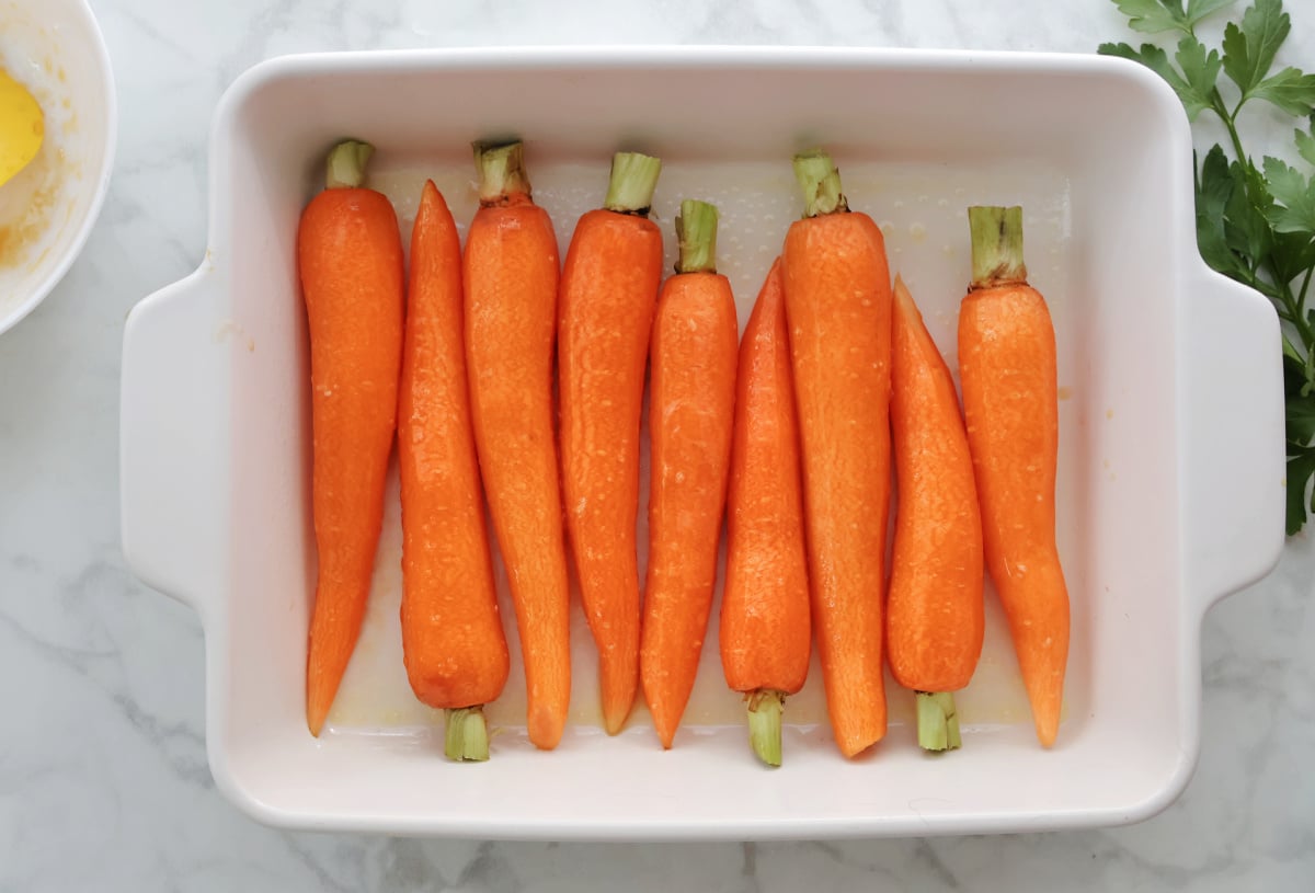 carrots ready to be roasted in a white roasting pan.