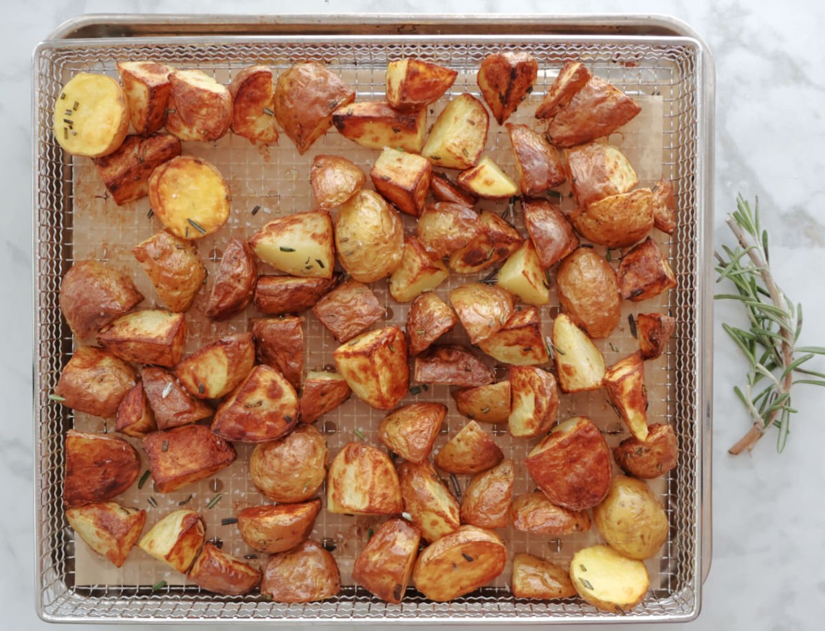 Pan of beautifully browned air fried rosemary potatoes with a light sprinkle of minced rosemary on top.