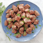 A plate of steak bites garnished with small pieces of parsley. The Montreal Steak Seasoning and the juices of the steak are visible on the blue serving plate.