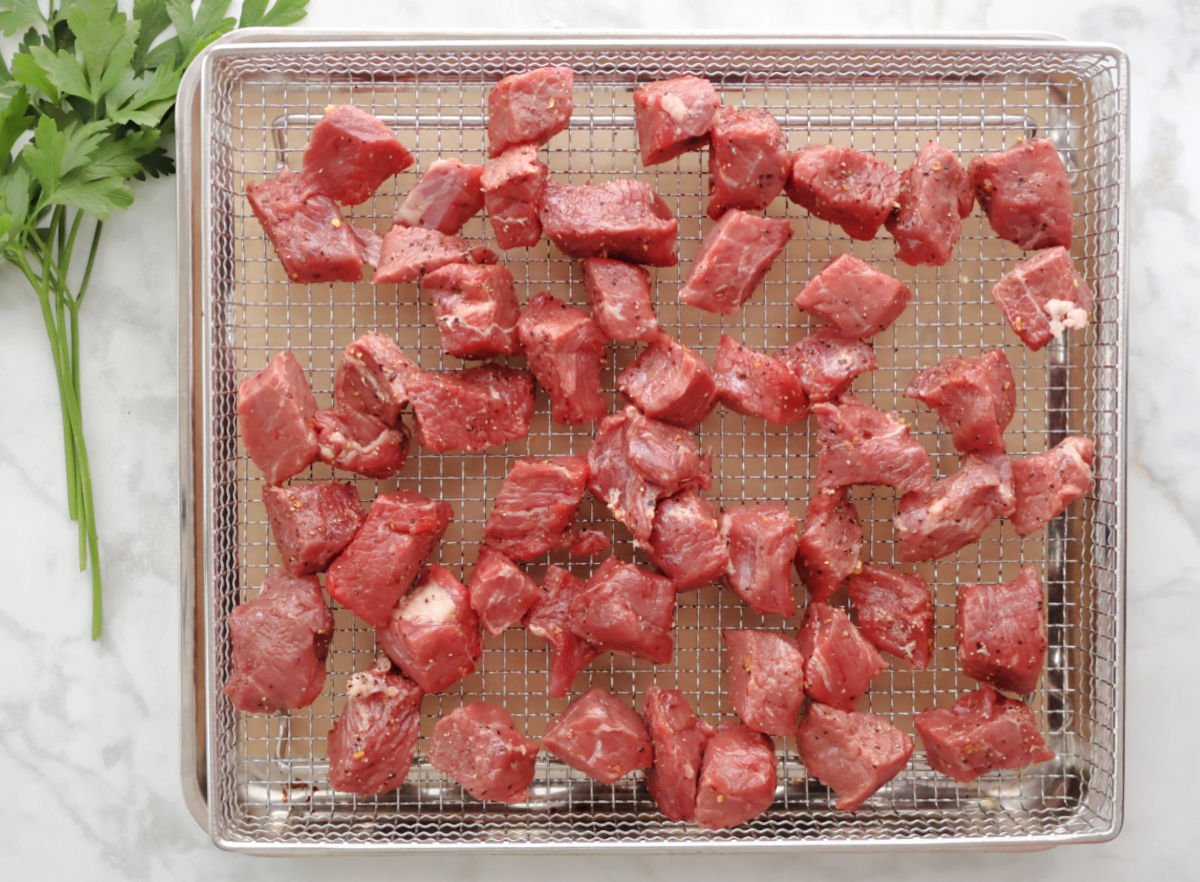 bite sized steak pieces spread on an air fryer basket.