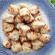 Air fryed chicken bites, browned in the air fryer and seasoned with Italian Seasonings. On a white and blue plate.