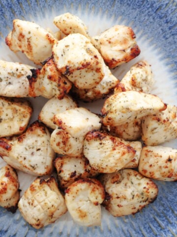 Air fryed chicken bites, browned in the air fryer and seasoned with Italian Seasonings. On a white and blue plate.