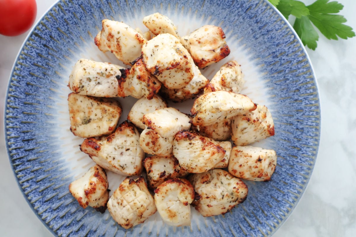 Air fryed chicken bites, browned in the air fryer and seasoned with Italian Seasonings. On a white and blue plate.