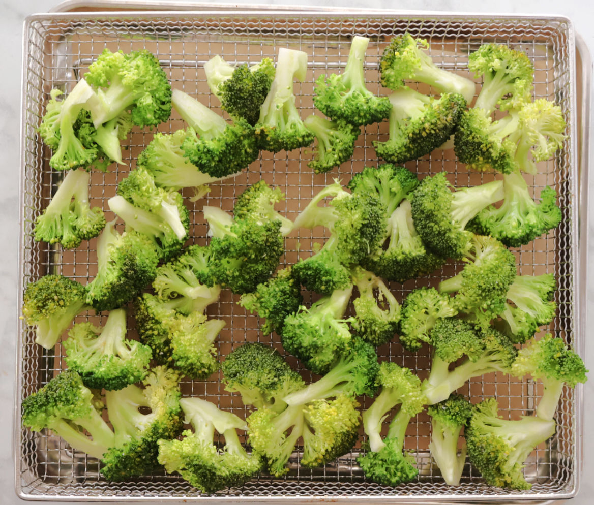 seasoned broccoli pieces on an air frier basket.