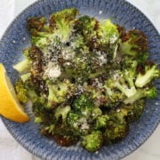 air fried broccoli with a sprinkling of parmesan cheese and a drizzle of lemon. Lemon wedge is to the side of the broccoli and it is all served on a blue plate.