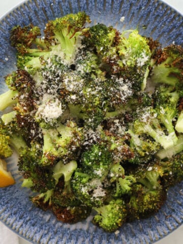 air fried broccoli with a sprinkling of parmesan cheese and a drizzle of lemon. Lemon wedge is to the side of the broccoli and it is all served on a blue plate.