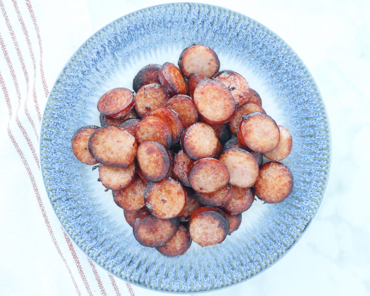 Cut coin style pieces of kielbasa with crispy edges cooked in an air fryer. On a blue plate.