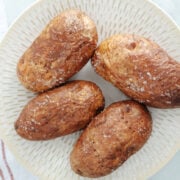 4 air fried baked potatoes with salt crystals on the skin on a white plate.