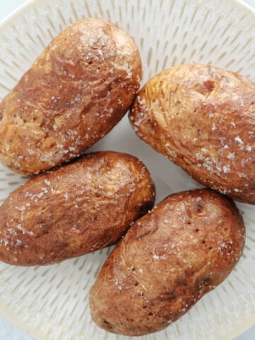 4 air fried baked potatoes with salt crystals on the skin on a white plate.