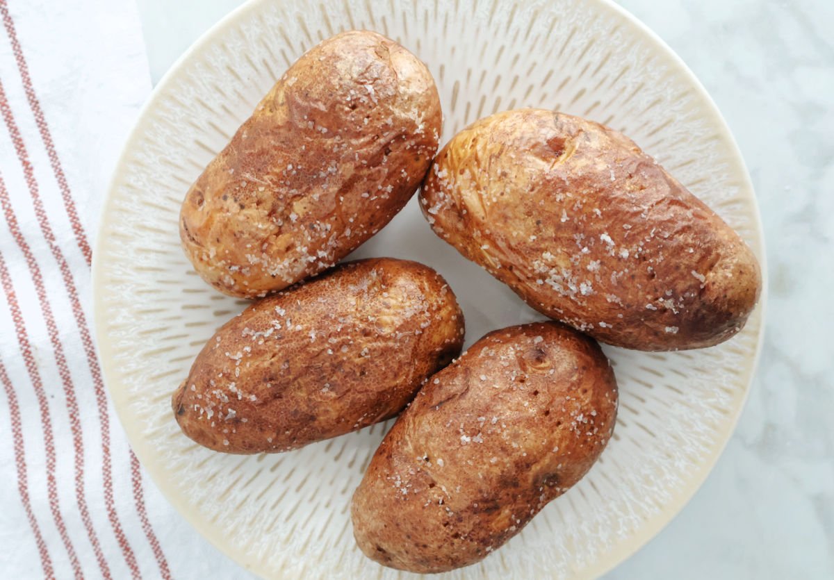 4 air fried baked potatoes with salt crystals on the skin on a white plate.