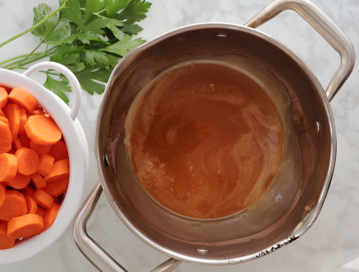 saucepan with butter and honey melted and combined. A colander with cooked carrots is also on the counter.