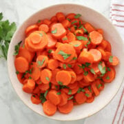 sliced carrots garnished with parsley in a white bowl.