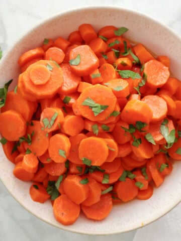 sliced carrots garnished with parsley in a white bowl.