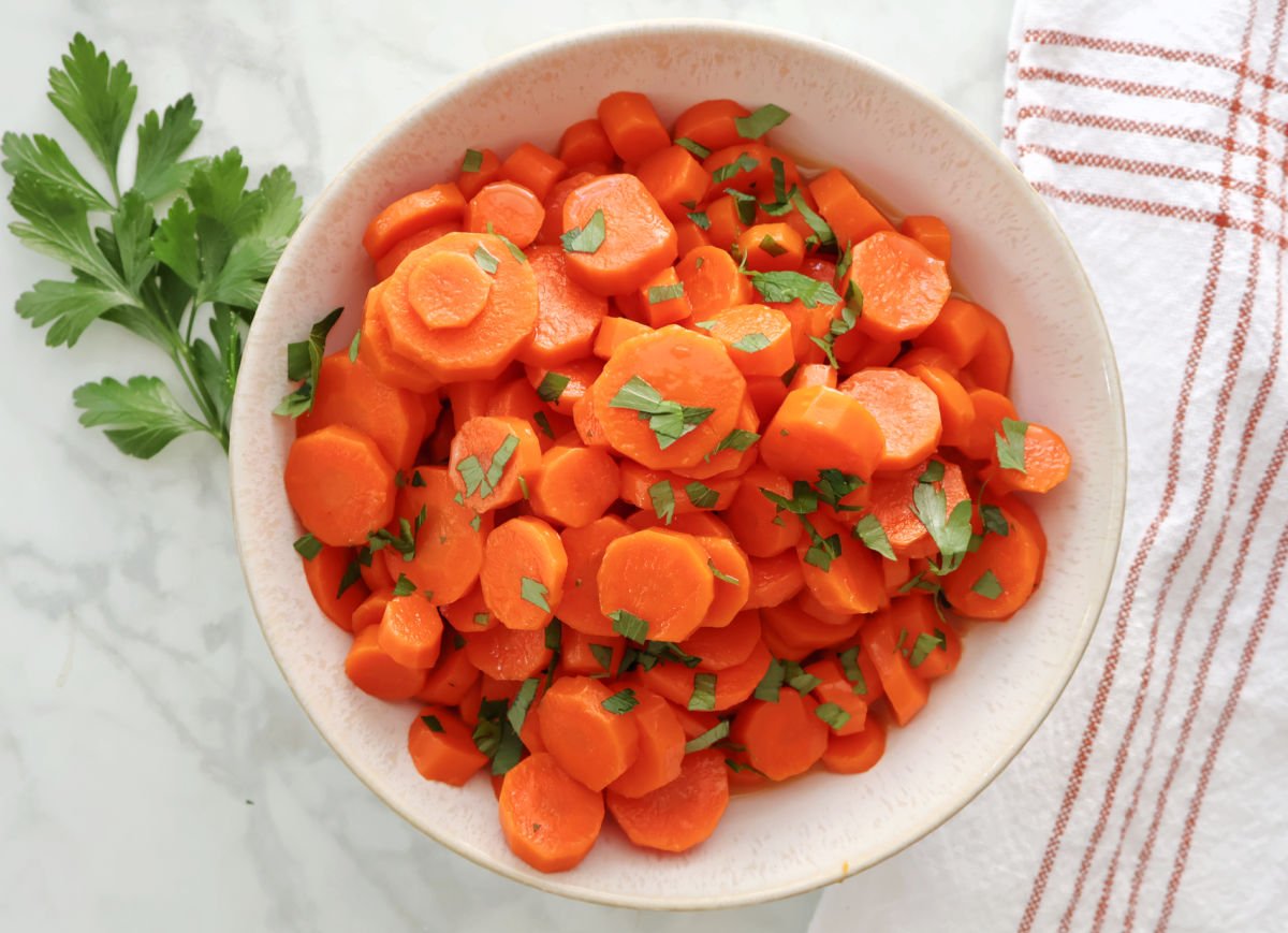 sliced carrots garnished with parsley in a white bowl.