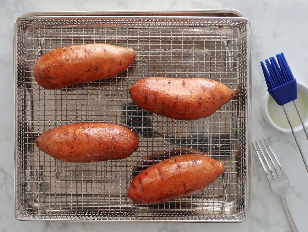 4 sweet potatoes with a coating of oil on an air fryer basket