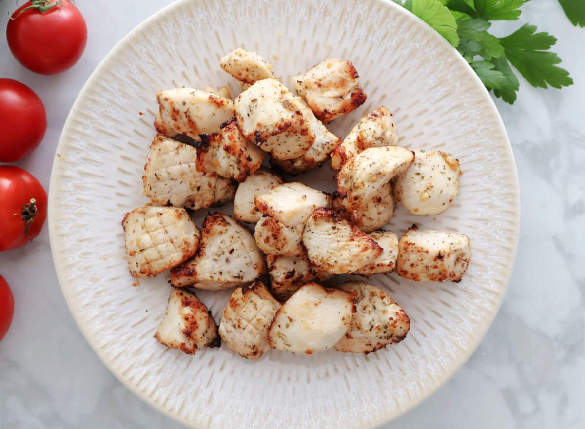 plate of air fried chicken bites. small red tomatoes and fresh parsley sprigs can be seen on the counter.