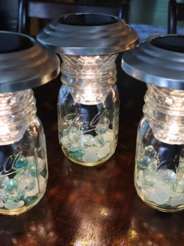 three solar lamps made with the top of landscaping solar lights and mason jars with marbles.