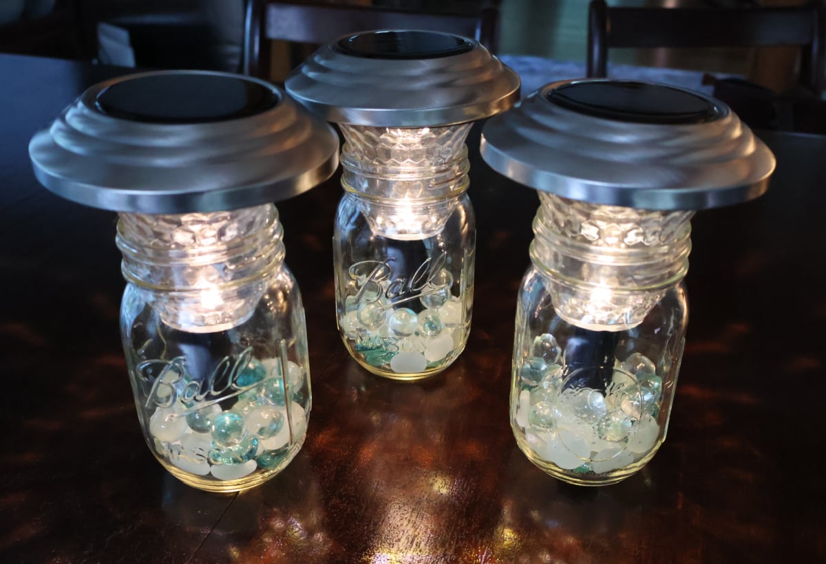 three solar lamps made with the top of landscaping solar lights and mason jars with marbles.