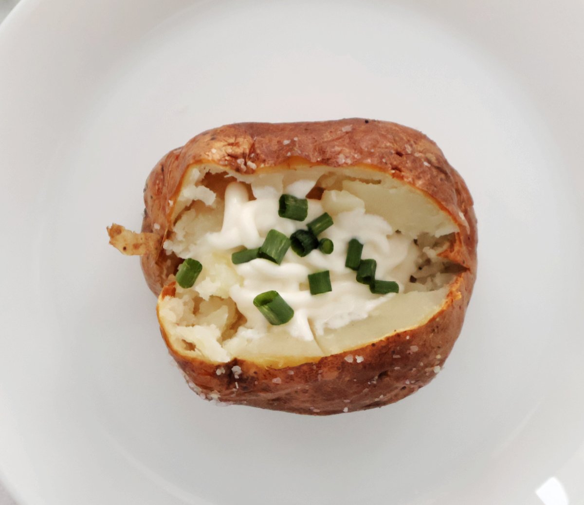 roasted air fryer potato split open with sour cream and chives as the toppingg.