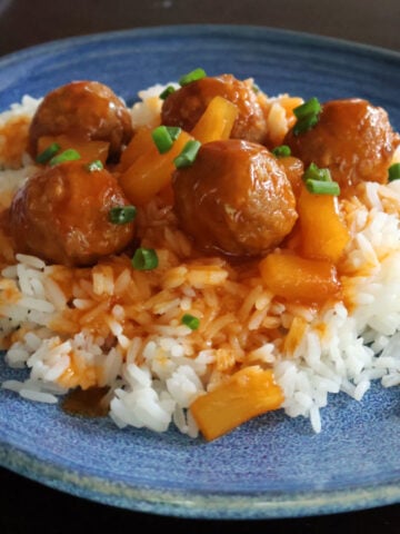 Meatballs on rice with a sweet and sour sauce drizzled on top of the meatballs and rice. Pineapple tidbits are visible in the sauce.